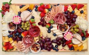 A tray of cheese, fruits, dried fruits, vegetables, crackers and condiments