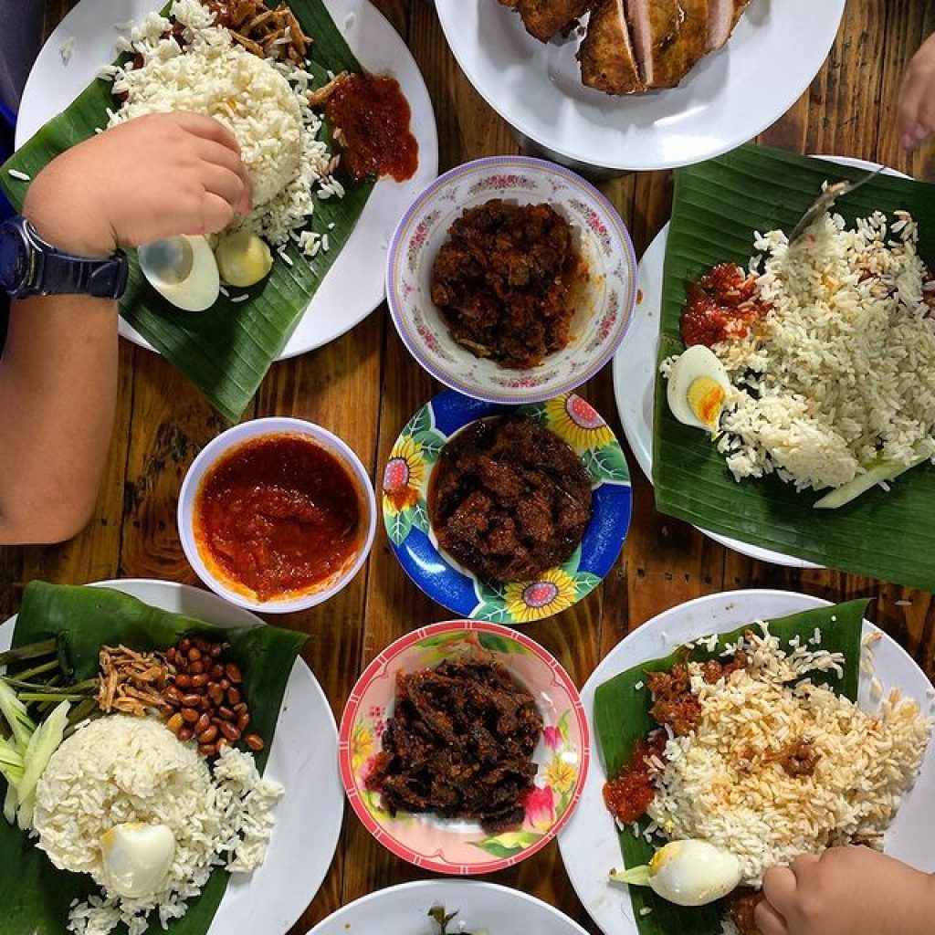 Malaysians eating nasi lemak with different dishes using their hands.