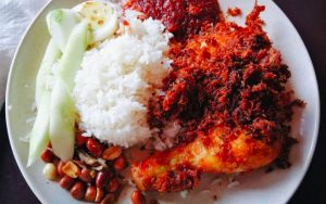 cooked rice served with fried chicken drumstick, fried peanuts, anchovies, hard boiled egg and sliced cucumber