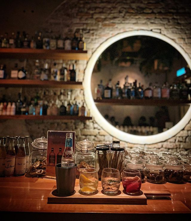 three different cocktails with a bottle of soda served on top of a bar