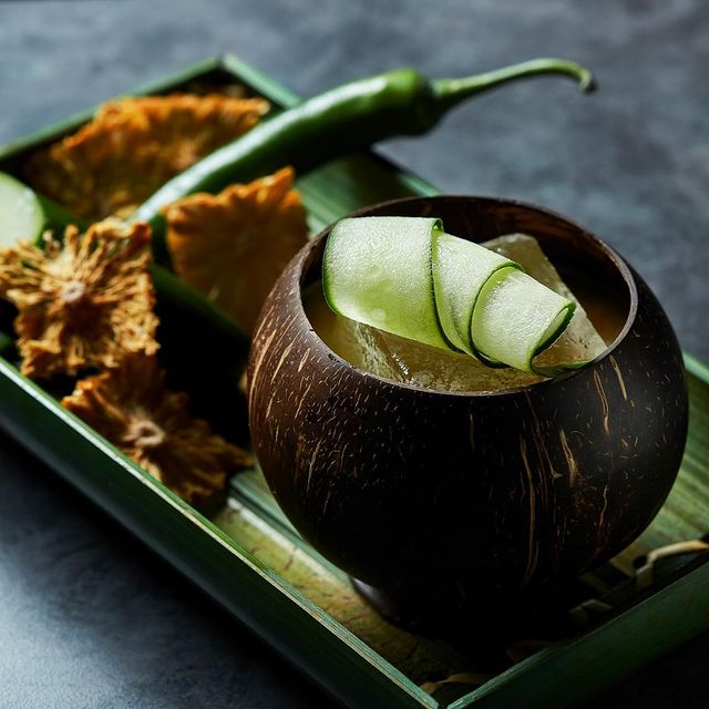 cocktail drink serve in a coconut shell with cucumber