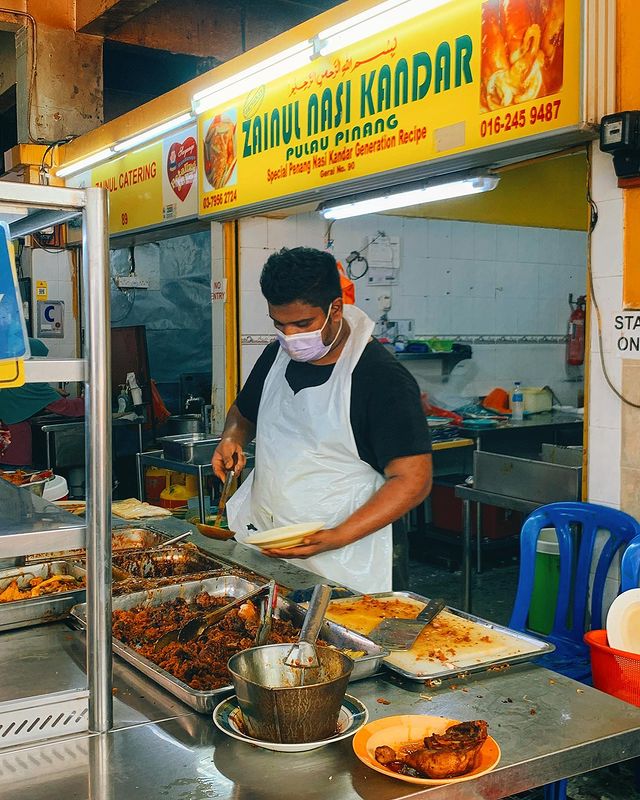 a nasi kandar restaurant crew scooping dishes and curries on a plate with rice