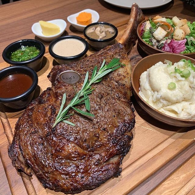 a grilled tomahawk steak garnished with fresh rosemary and served together with mashed potatoes and salads