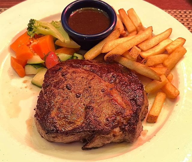 steak served with french fries, salads and sauce on a round white plate