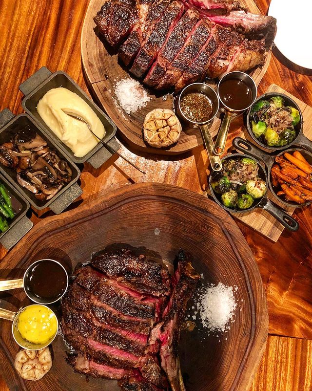 slices of grilled steak served with vegetables, mushrooms, garlic, mashed potatoes and different type of sauces