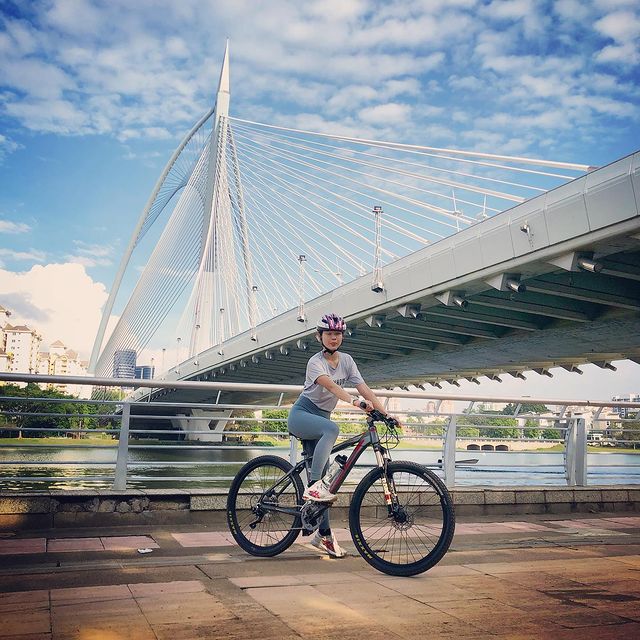 A lady on a bicycle in front of a bridge in a city