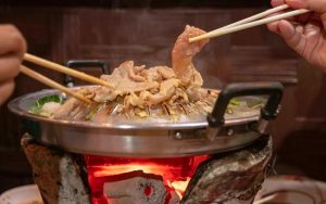 hands holding chopstick while cooking strips of meat on a mookata