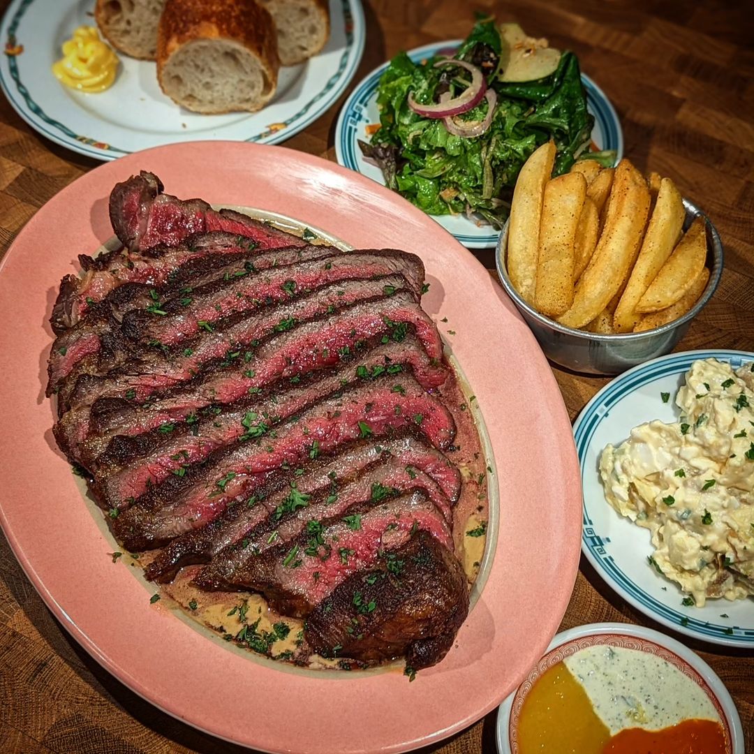 Sliced cooked meat with such dishes such as potatoes, leafy vegetables and bread served on a table
