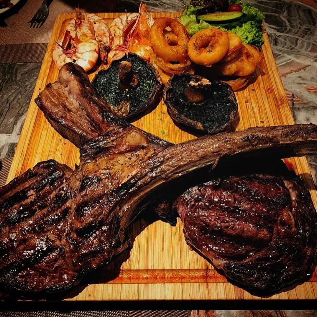 grilled tomahawk steak with shrimp, calamari, mushrooms and salad served on a wooden board