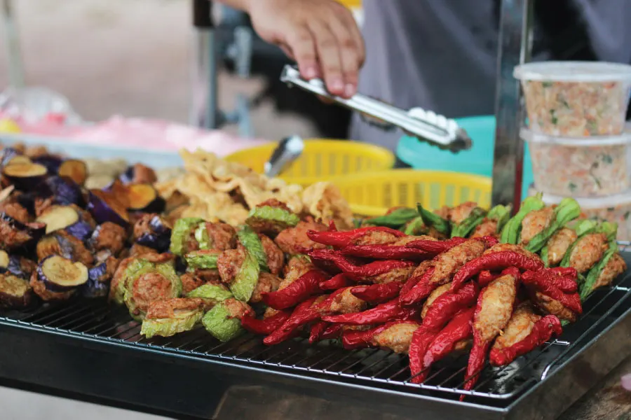 a hand holding a metal tongs in front of fried foods