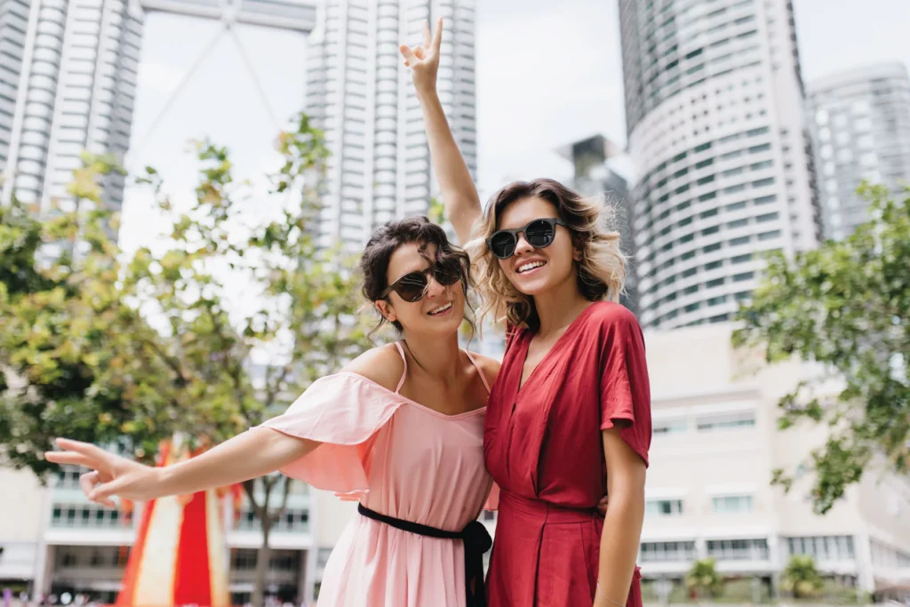 two female tourists wearing sunglasses posing for photos in a city