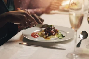 hands holding fork and knife to cut a dish that is served on a plate