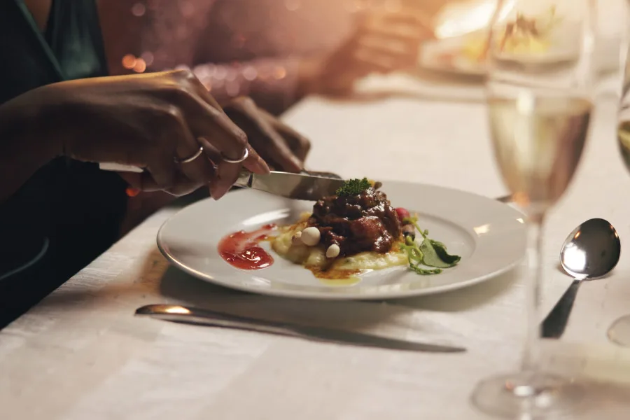 hands holding fork and knife to cut a dish that is served on a plate