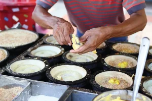 man slicing banana on half cooked apam balik on the pan