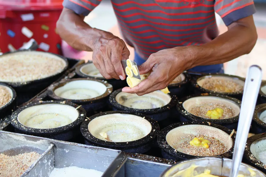 man slicing banana on half cooked apam balik on the pan