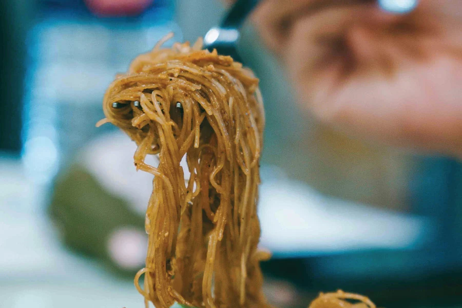 a hand holding a fork scooping noodles