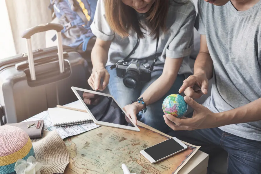 a couple sitting with maps, tablets and smartphone planning to travel