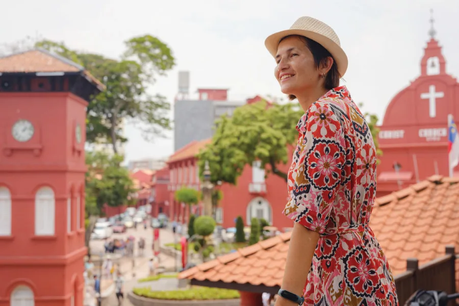 woman with a hat looking ahead towards red coloured buildings