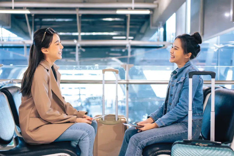 two women smiling and chatting with each other at the airport terminal