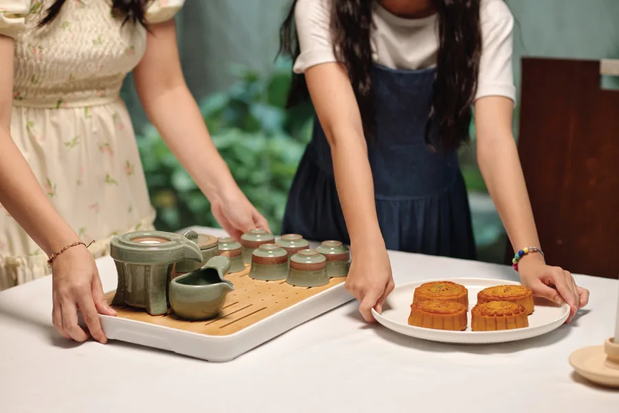 two ladies serving mooncakes and teas on a table