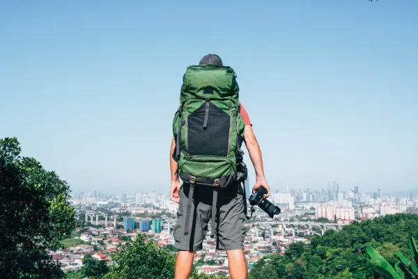 man with backpack holding a camera overlooking a city from a higher spot